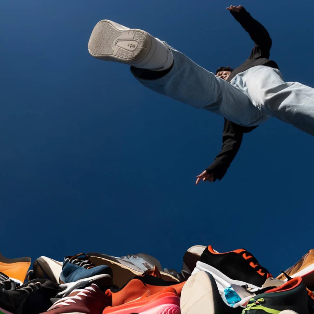 Women wearing plant-based shoes jumping pile of waste sneakers